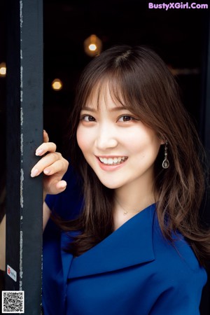 A woman in a blue dress leaning against a pole.