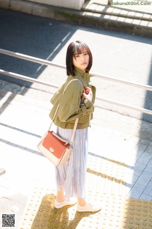 A woman in a white sweater and blue skirt is walking down the street.