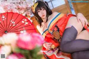 A woman in a red and black kimono sitting on a bed.
