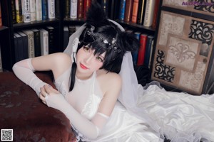 A woman in a wedding dress sitting in front of a bookshelf.