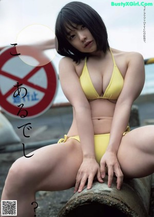 A woman in a black bra sitting on a bed.
