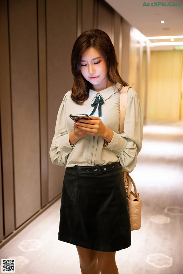 A woman in a white shirt and black skirt looking at her phone.