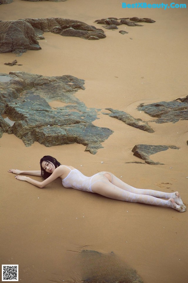 A woman laying on a sandy beach next to rocks.