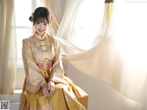A woman in a kimono sitting on a bed next to a window.