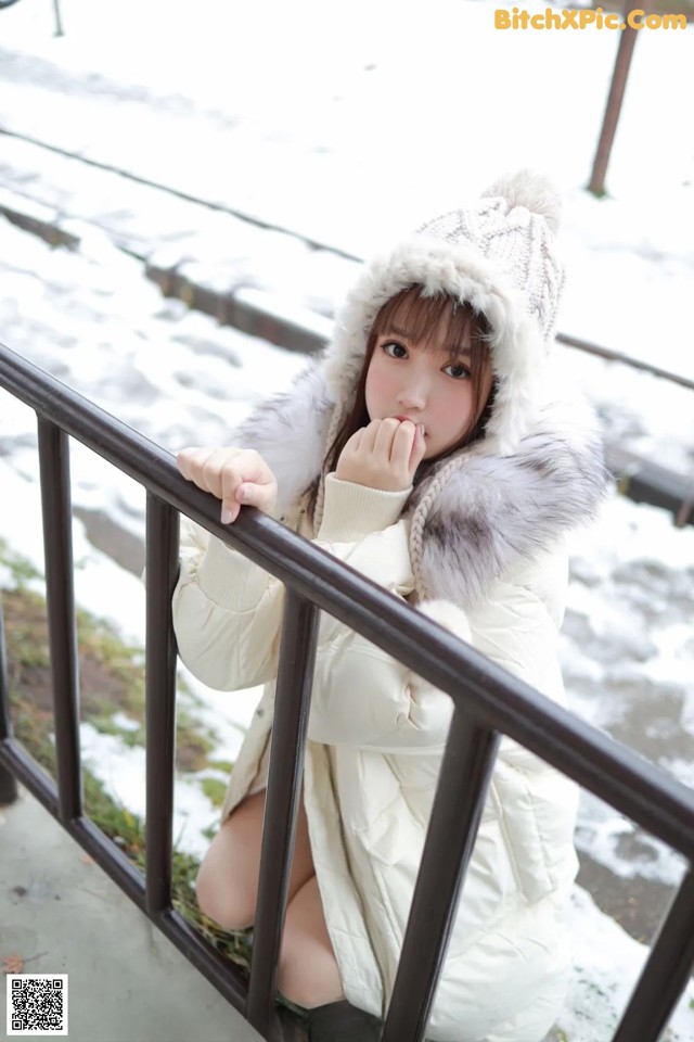 A woman in a white coat and hat sitting on a railing.