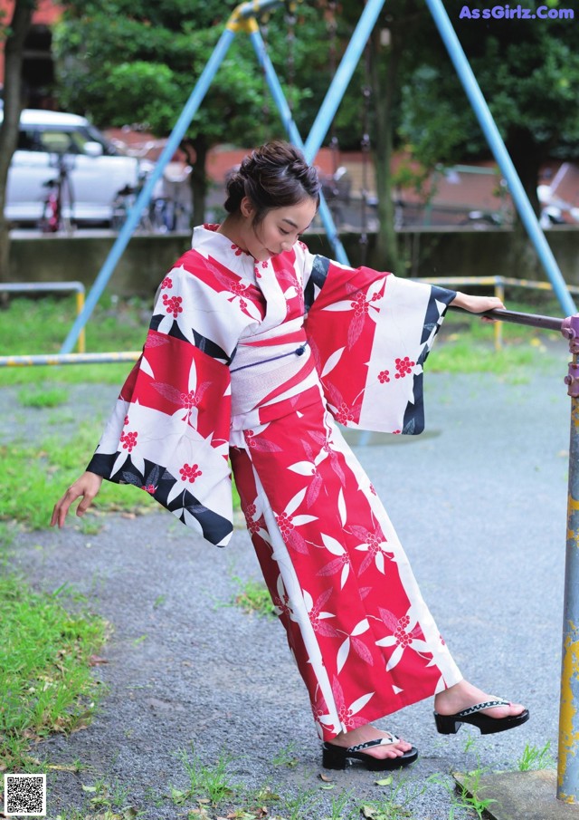 A woman in a red and white kimono standing next to a pole.