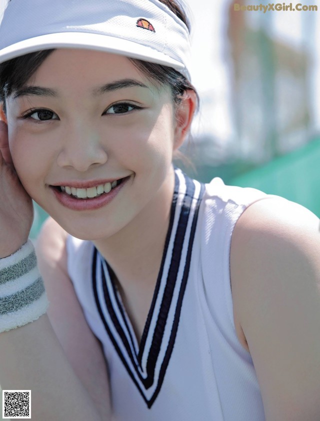 A young woman wearing a white tennis outfit and a white hat.