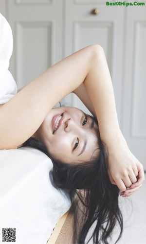 A woman with long black hair laying on a bed.