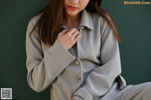 A woman in a gray shirt and black shorts leaning against a wall.